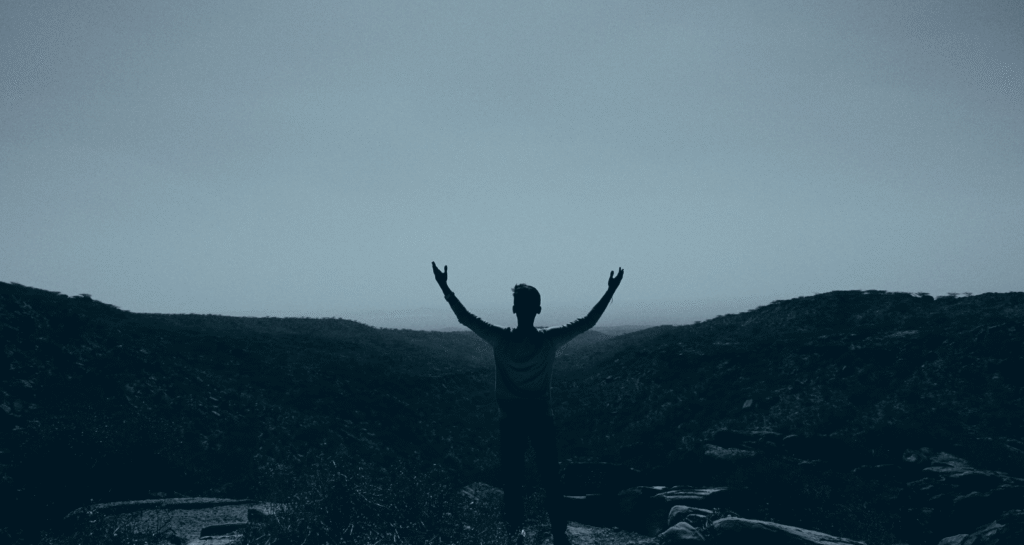 Person with raised arms overlooking mountain valley.